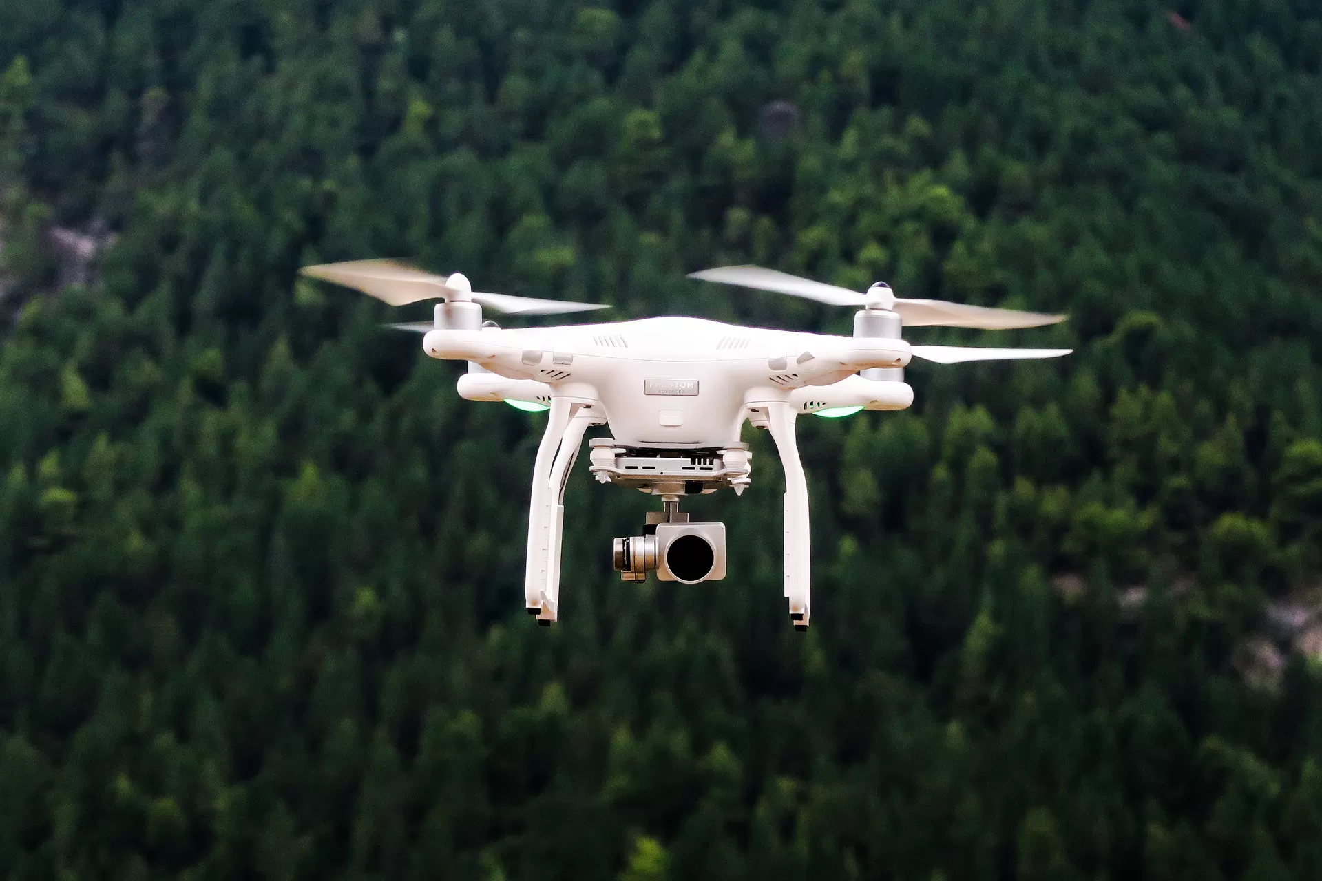Eine weisse Drohne mit Kamera fliegt über ein Waldgebiet.