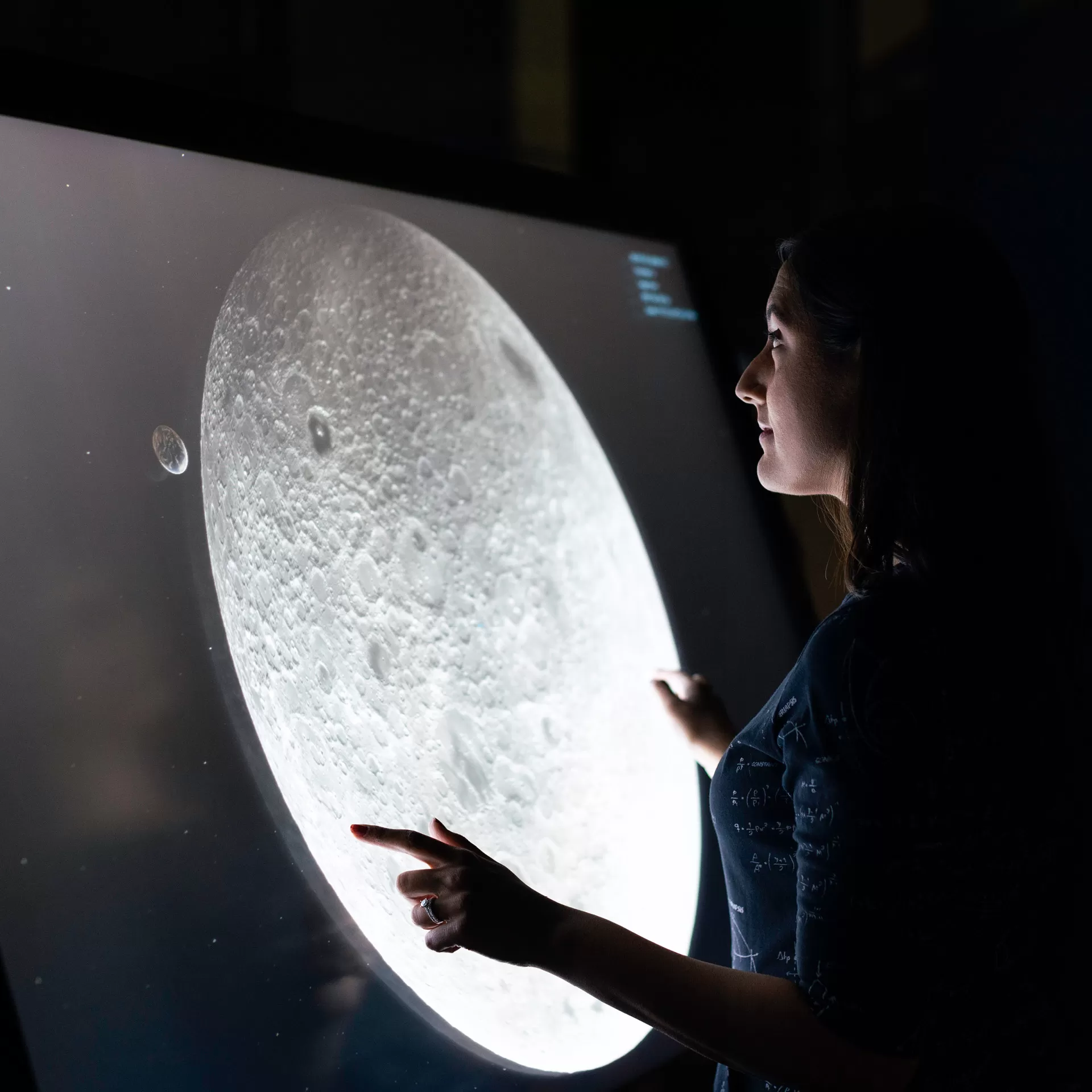Eine Ingenieurin für Raumfahrtoperationen betrachtet den Mond auf einem grosen Touchscreen.