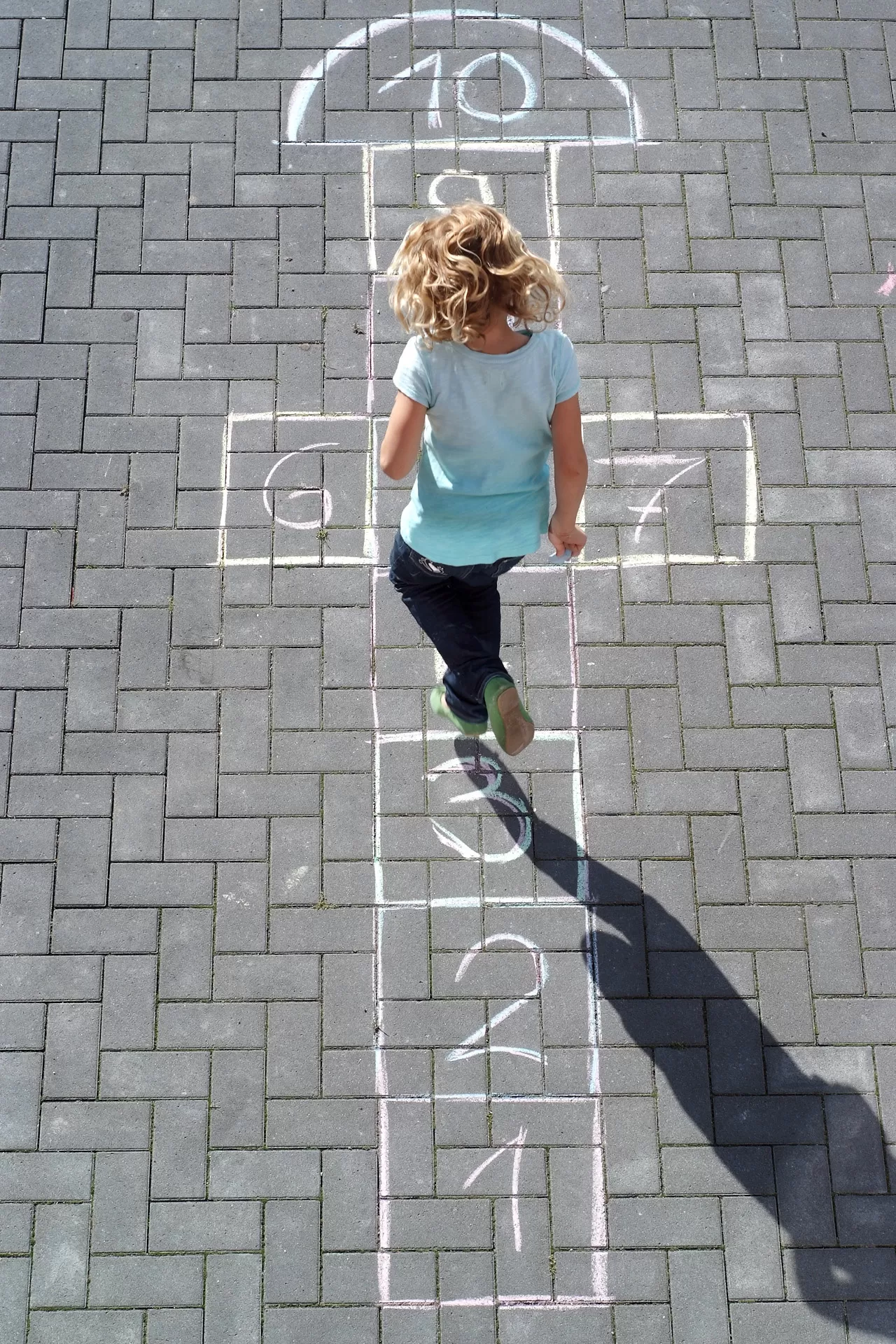 Kind hüpft Himmel-und-Hölle-Spiel, das mit Kreide auf den Boden gemalt ist.