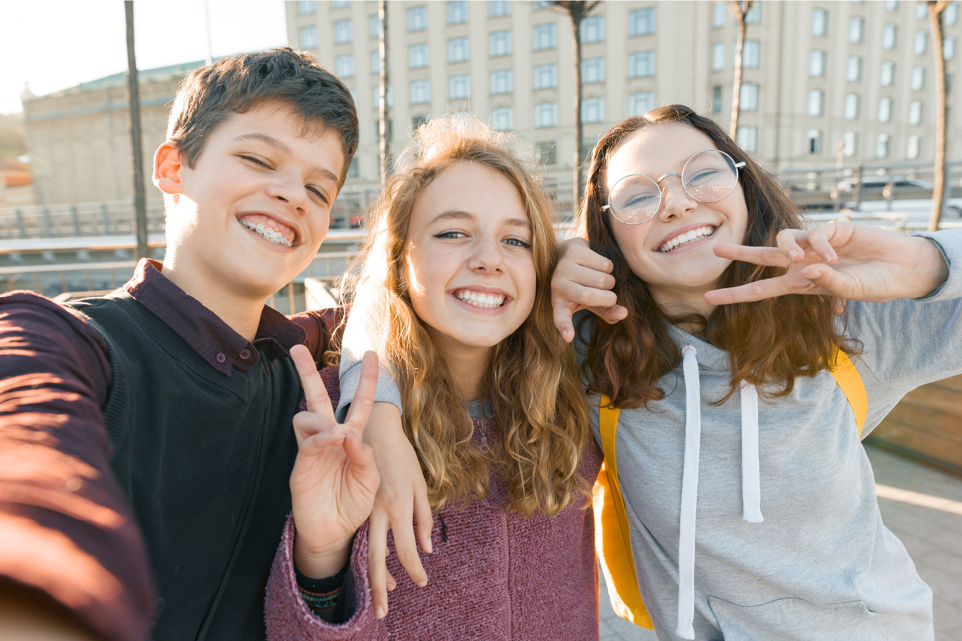 Selfie von drei fröhlichen Jugendlichen, die sich umarmen und mit den Händen das Peace-Zeichen machen.