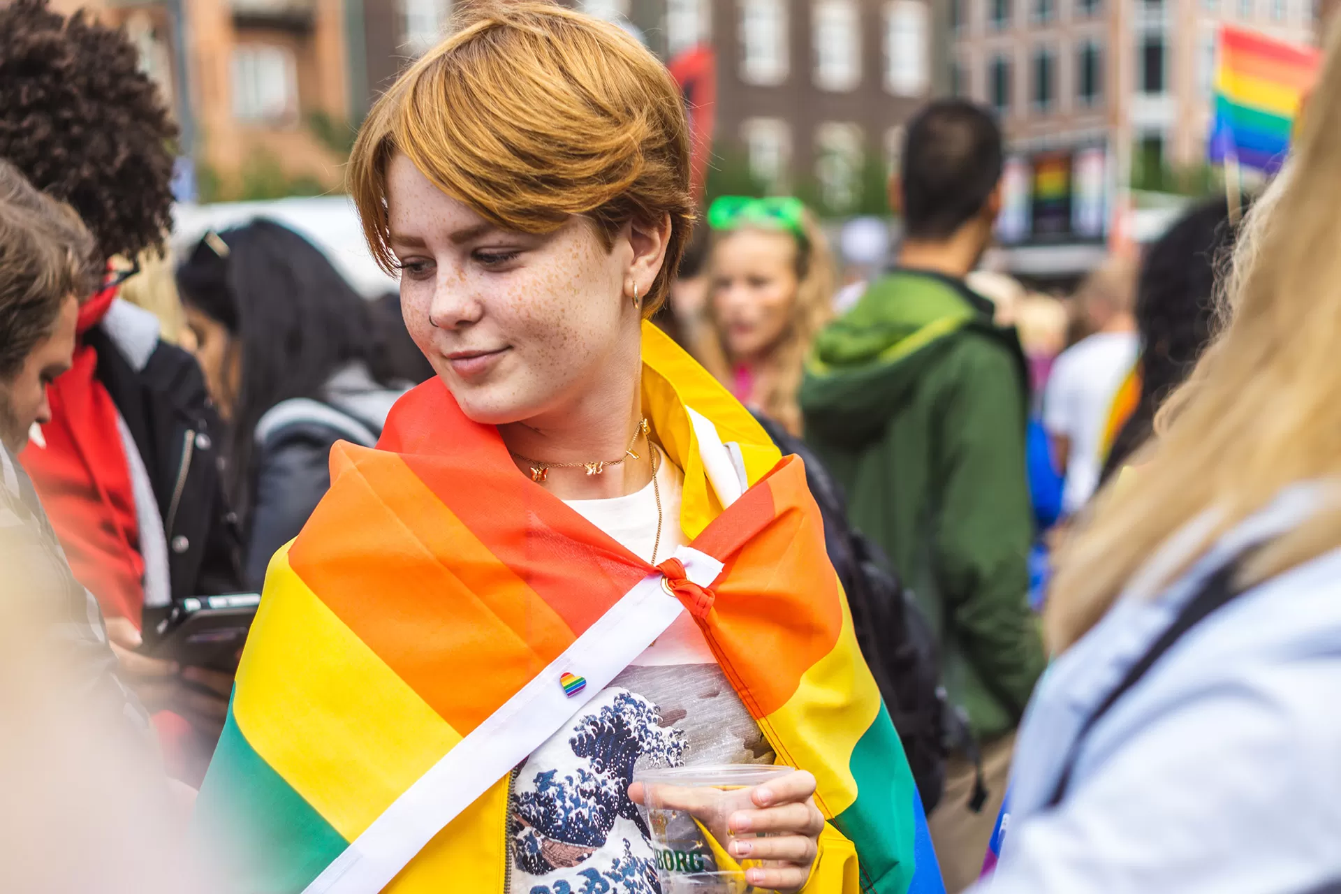 Eine junge Frau trägt eine Regenbogenflagge um die Schultern an einer Kundgebung.