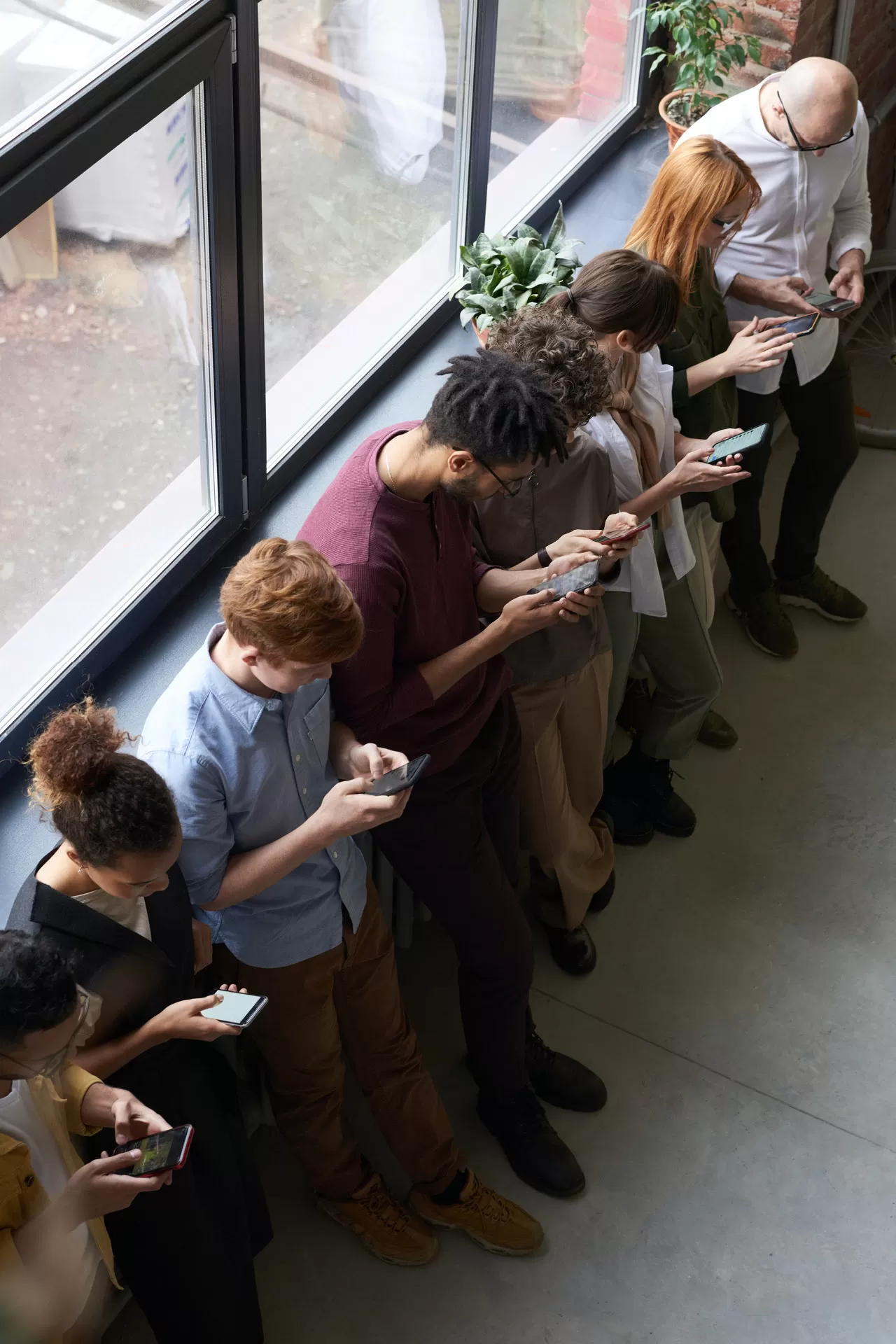 Eine Gruppe von jungen Leuten steht nebeneinander an eine Wand gelehnt und alle schauen auf ihr Smartphone.