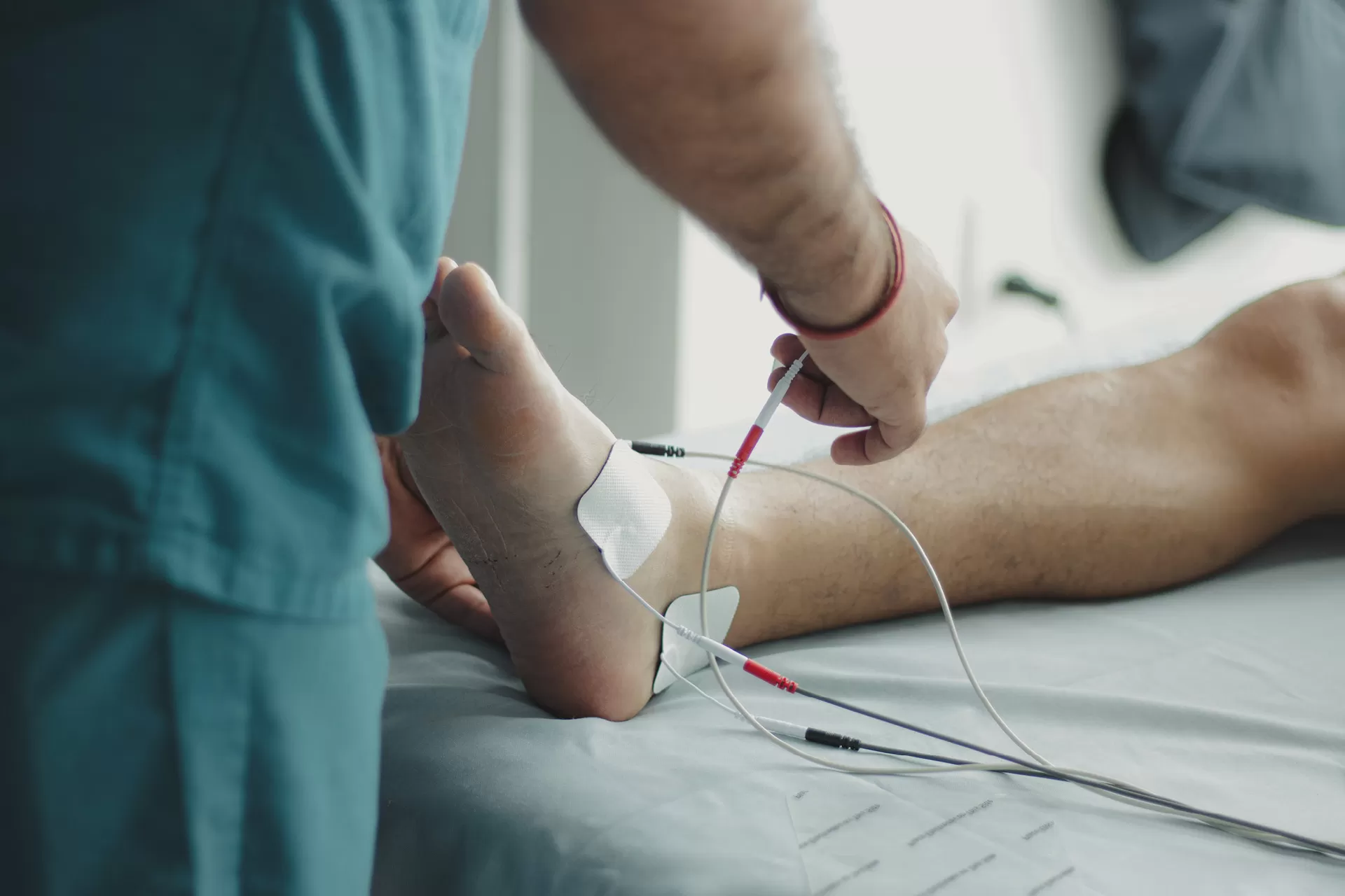 Rehabilitation, der Arzt bringt Elektroden an Fuss eines Patienten an.