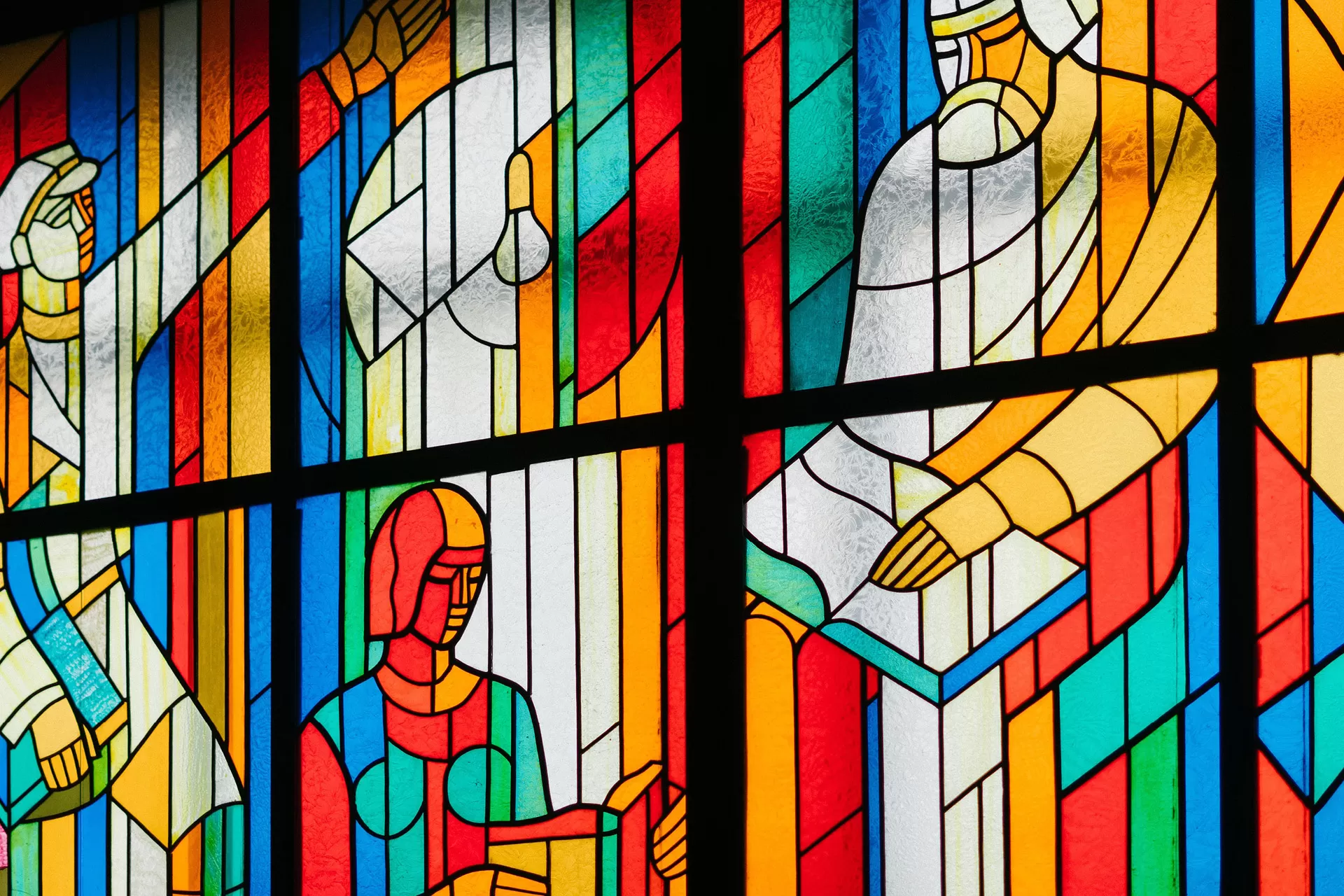 In einem Kirchenfester aus Buntglas sind lesende und diskutierende Personen dargestellt.