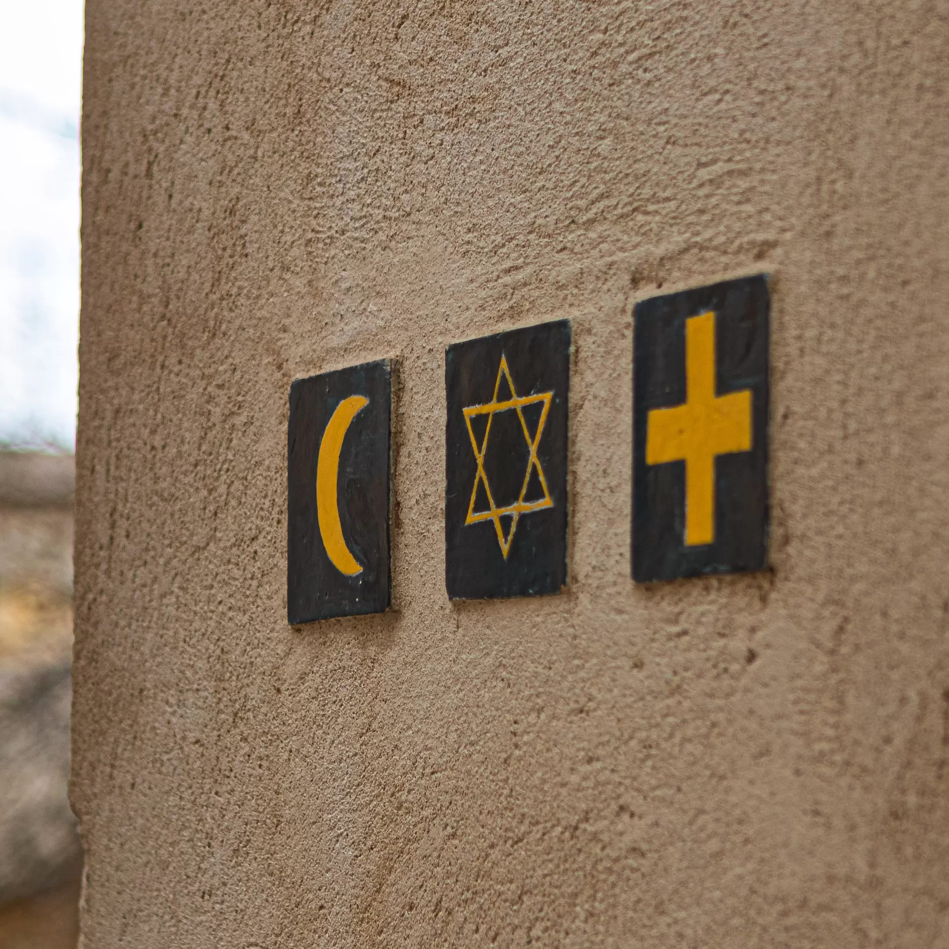 An einer Häuserwand sind drei Keramikkacheln befestigt mit den Symbolen von Islam, Judentum und Christentum.