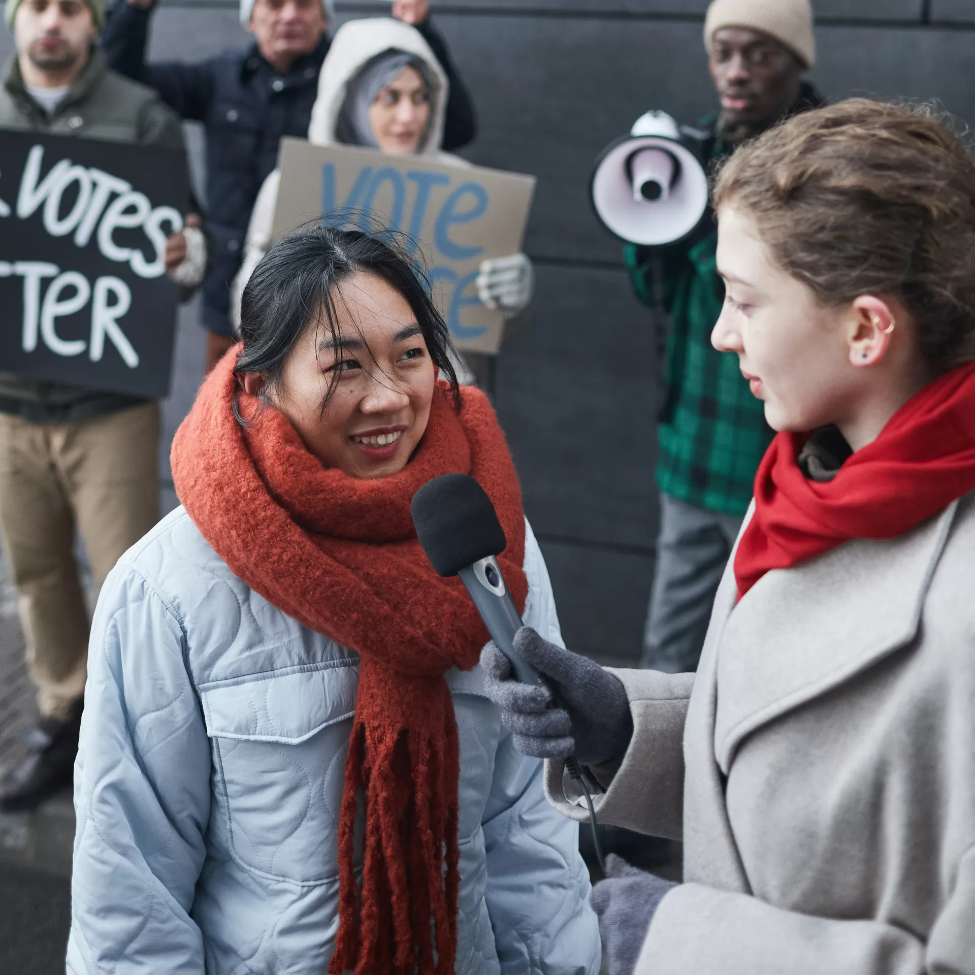 Eine Frau mit Mikrophon in der Hand interviewt eine Frau aus einer Demonstrantengruppe.