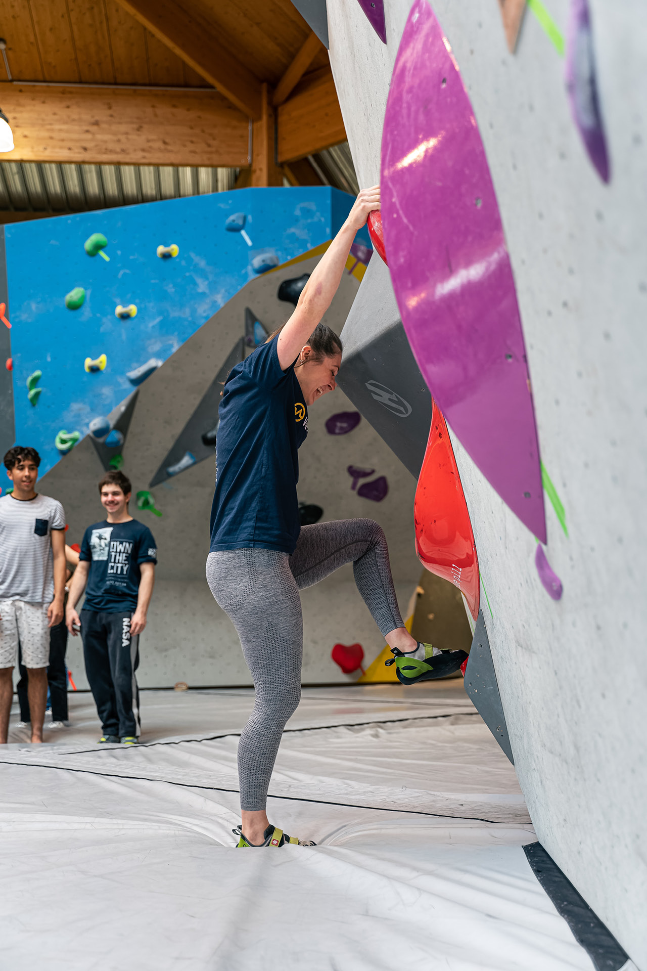 Eine junge Kletterin zeigt Jugendlichen in einer Boulderhalle Grifftechniken vor.