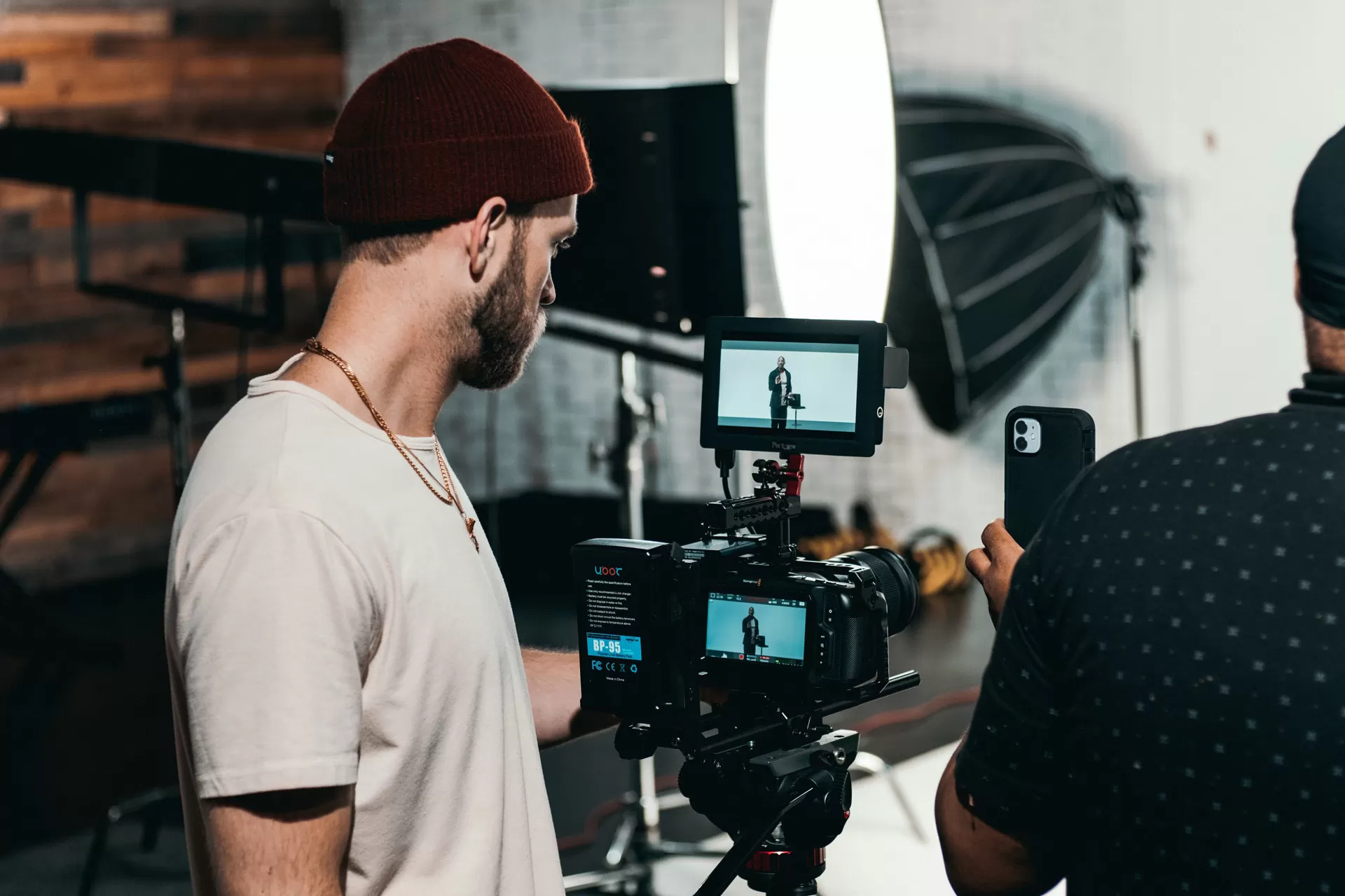 Ein Mann bedient eine Filmkamera während einer Aufnahme, ein zweiter Mann filmt gleichzeitig mit dem Smartphone.