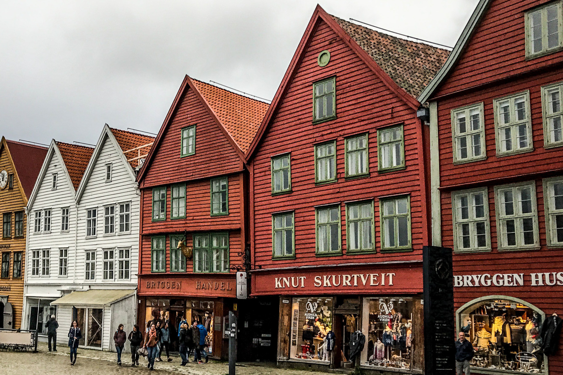 Eine Einkaufsstrasse in Bergen, Norwegen, mit typischen farbigen, alten Holzhäusern. Die Geschäfte sind beschriftet in norwegischer Sprache.