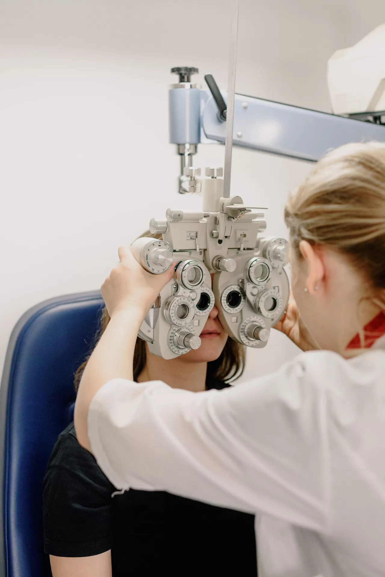 Optometristin misst mit dem Phoropter (augentechnisches Messgerät) die Sehleistungen der Augen einer Patientin.