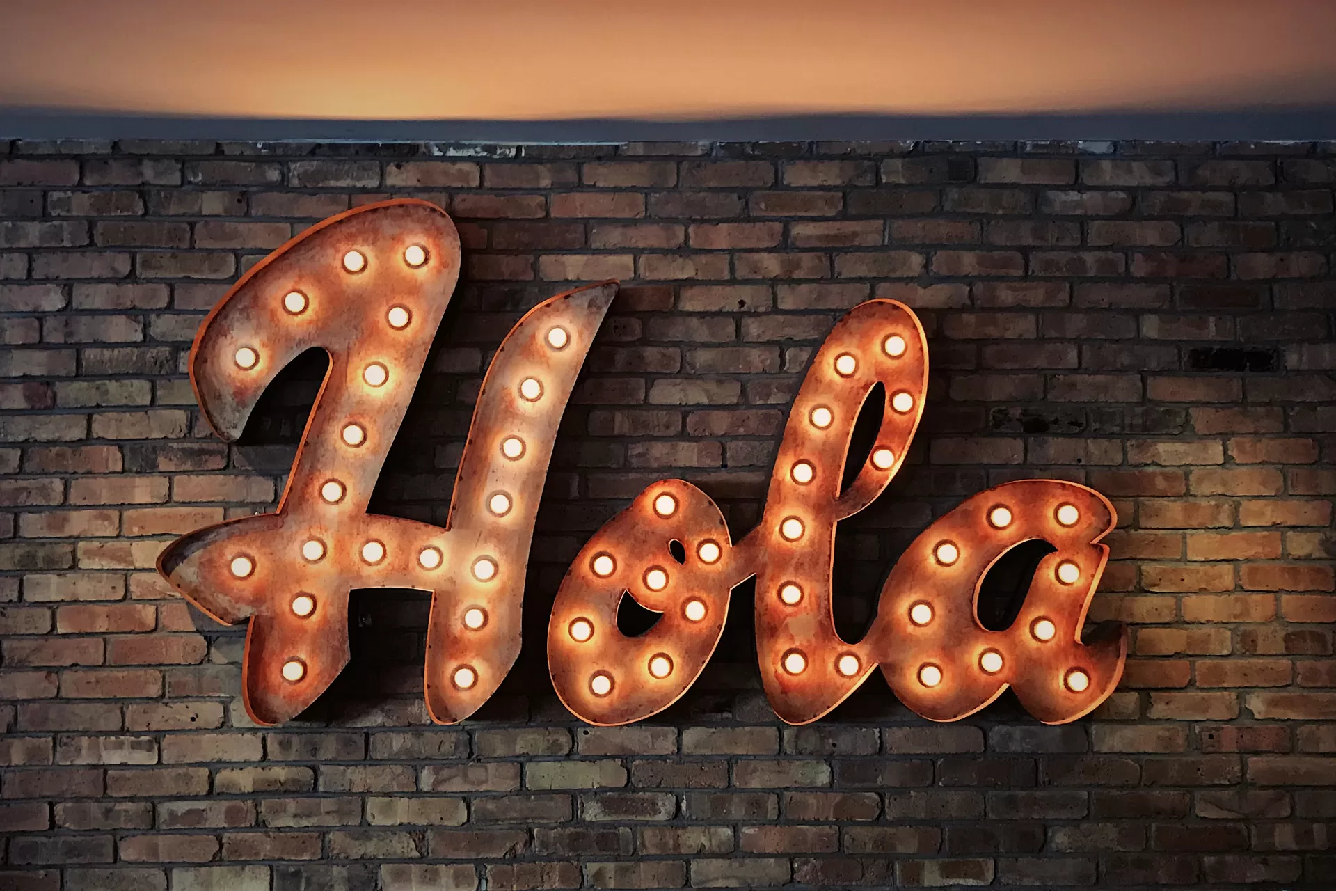 Das spanische Wort «Hola» hängt in grossen Leuchtbuchstaben an einer Backsteinmauer.
