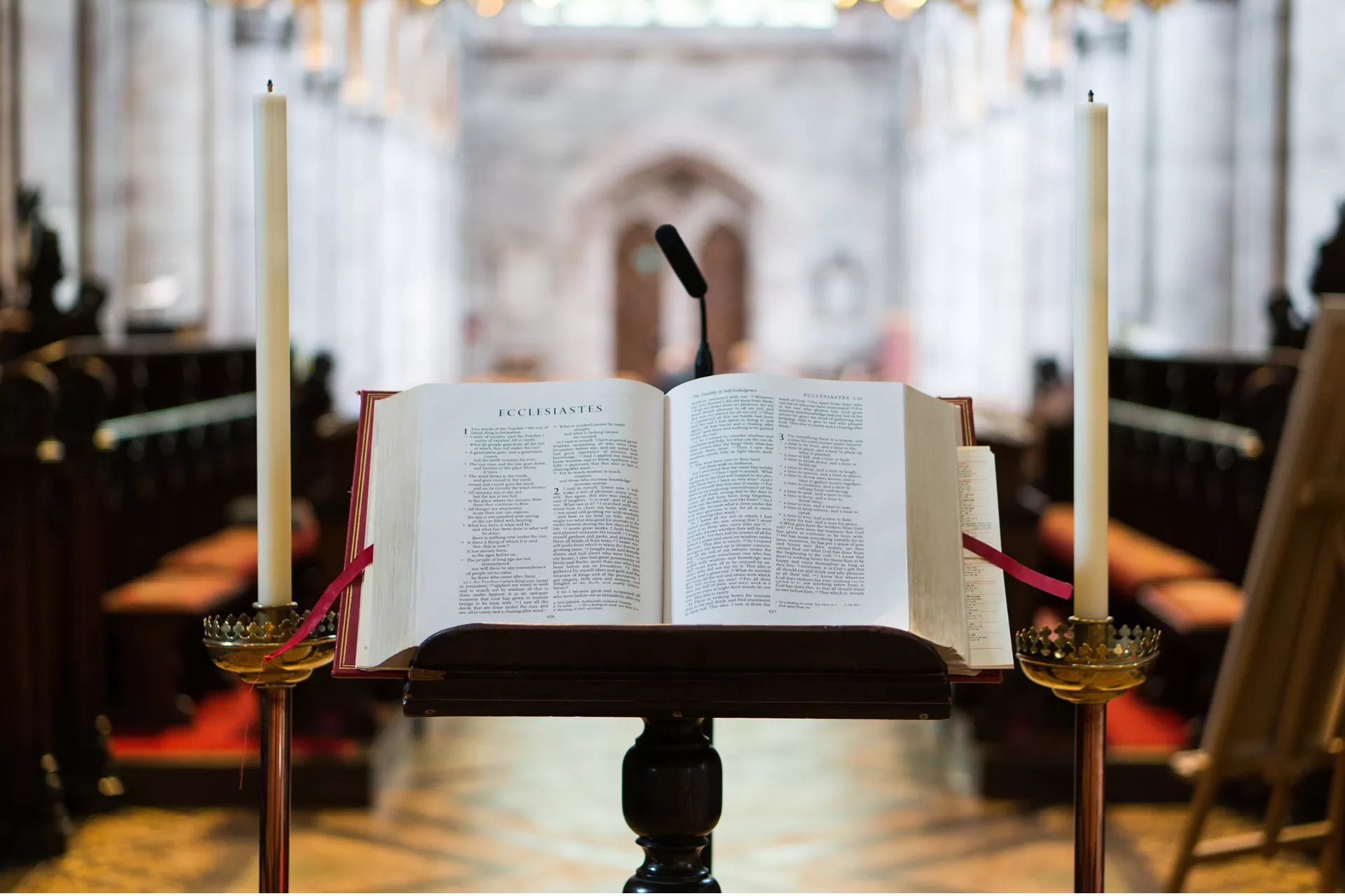 Eine offene Bibel liegt auf einem Buchständer in der Kirche, links und rechts davon ist eine Kerze aufgestellt.