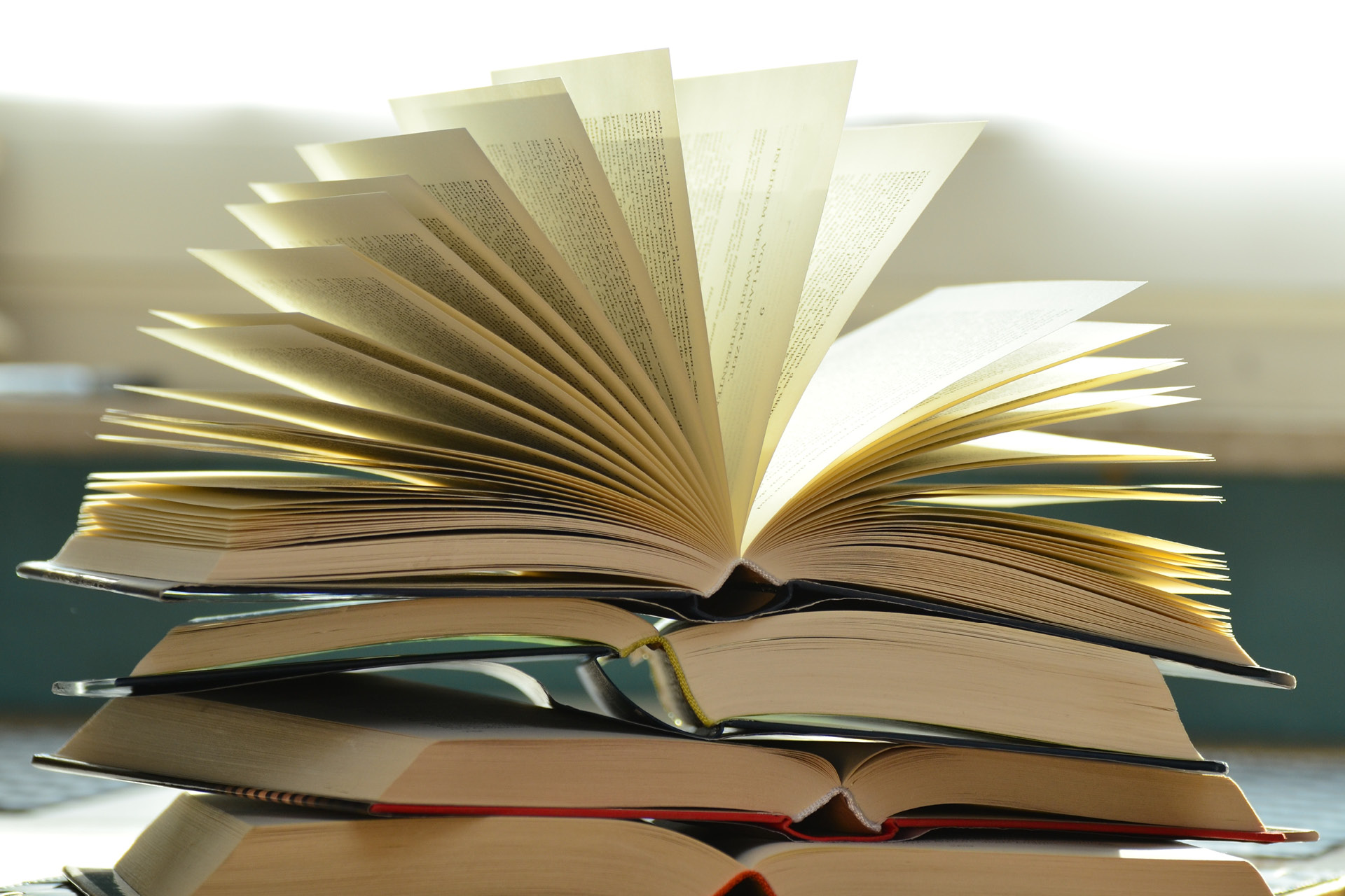 Ein Buch mit weit aufgefächerten Seiten liegt auf einem Stapel von aufgeschlagenen Büchern.