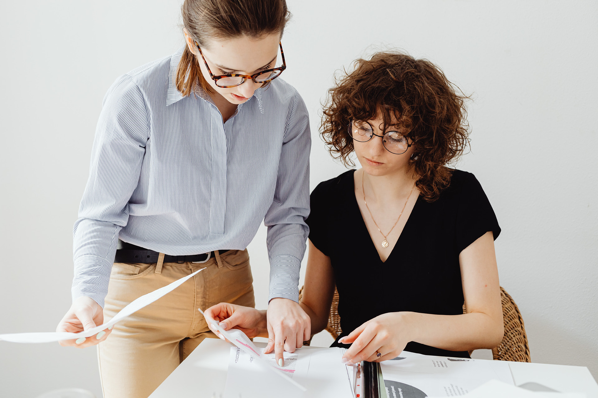 Zwei junge Geschäftsfrauen besprechen Unterlagen an einem Bürotisch.