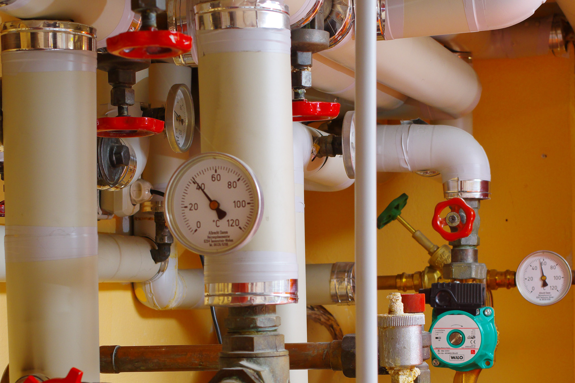 Detailaufnahme von Temepraturanzeigen, Leitungen und Handrädern eines Heizungssystemes.