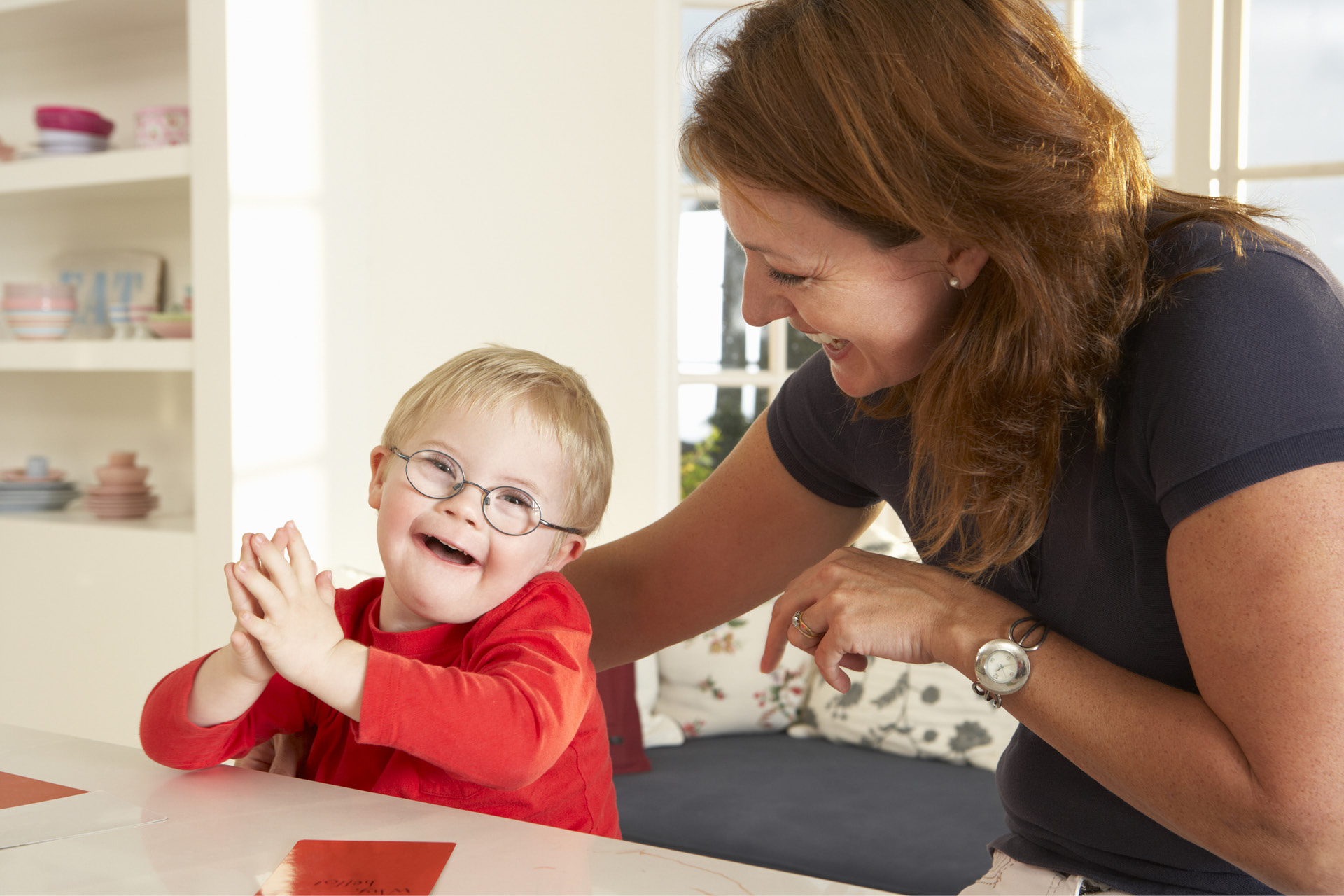 Ein kleiner Junge mit Down-Syndrom lacht mit seiner Therapeutin.
