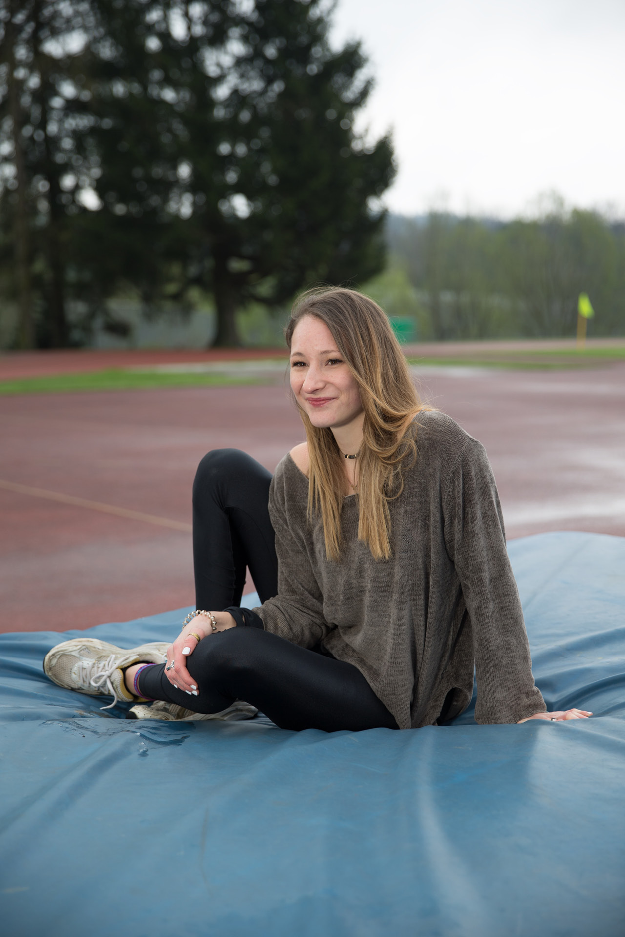 Eine junge Sportlerin sitzt auf einer dicken Matte auf dem Sportplatz.