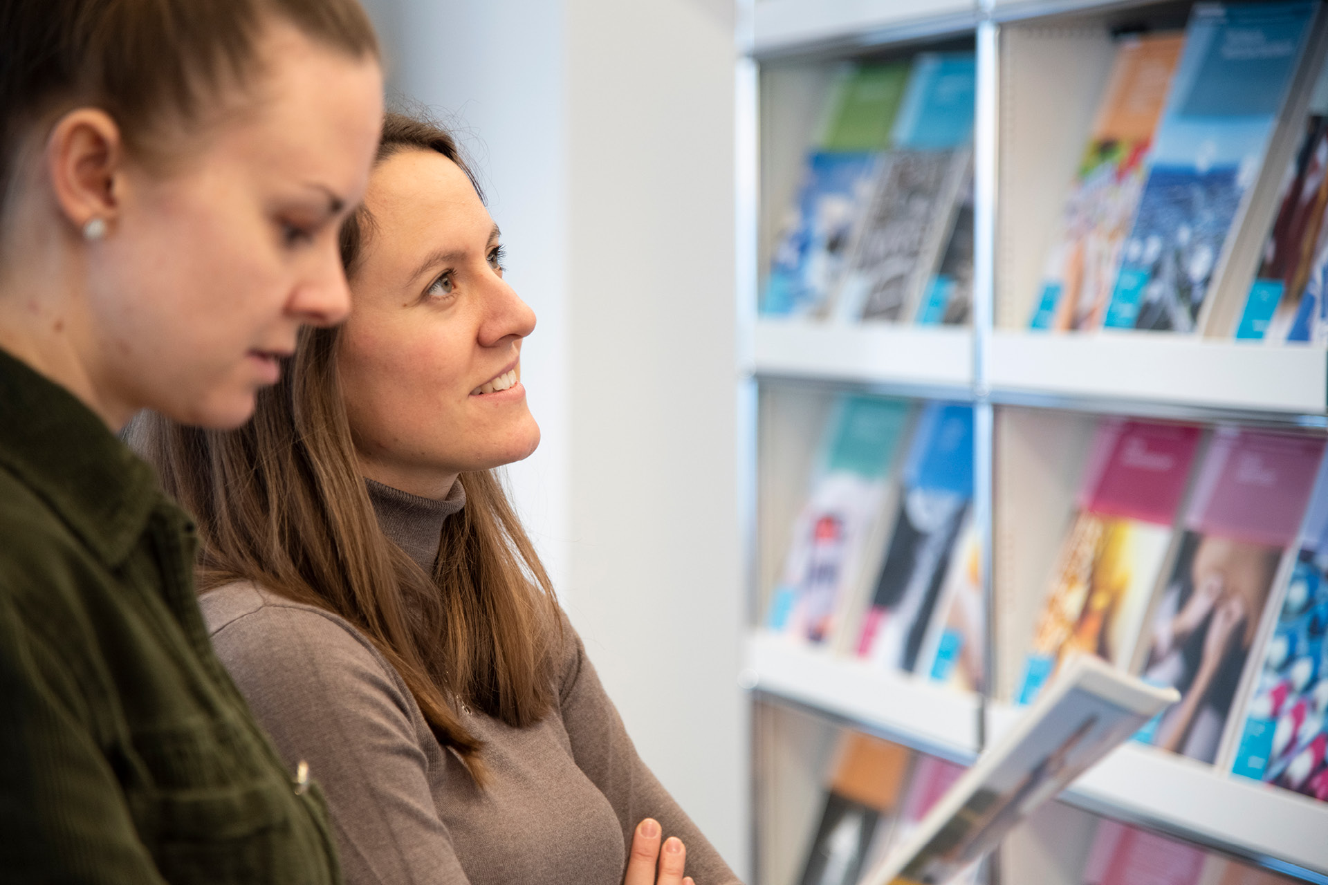 Zwei junge Frauen stehen vor einem Regal mit bunten Magazinen.