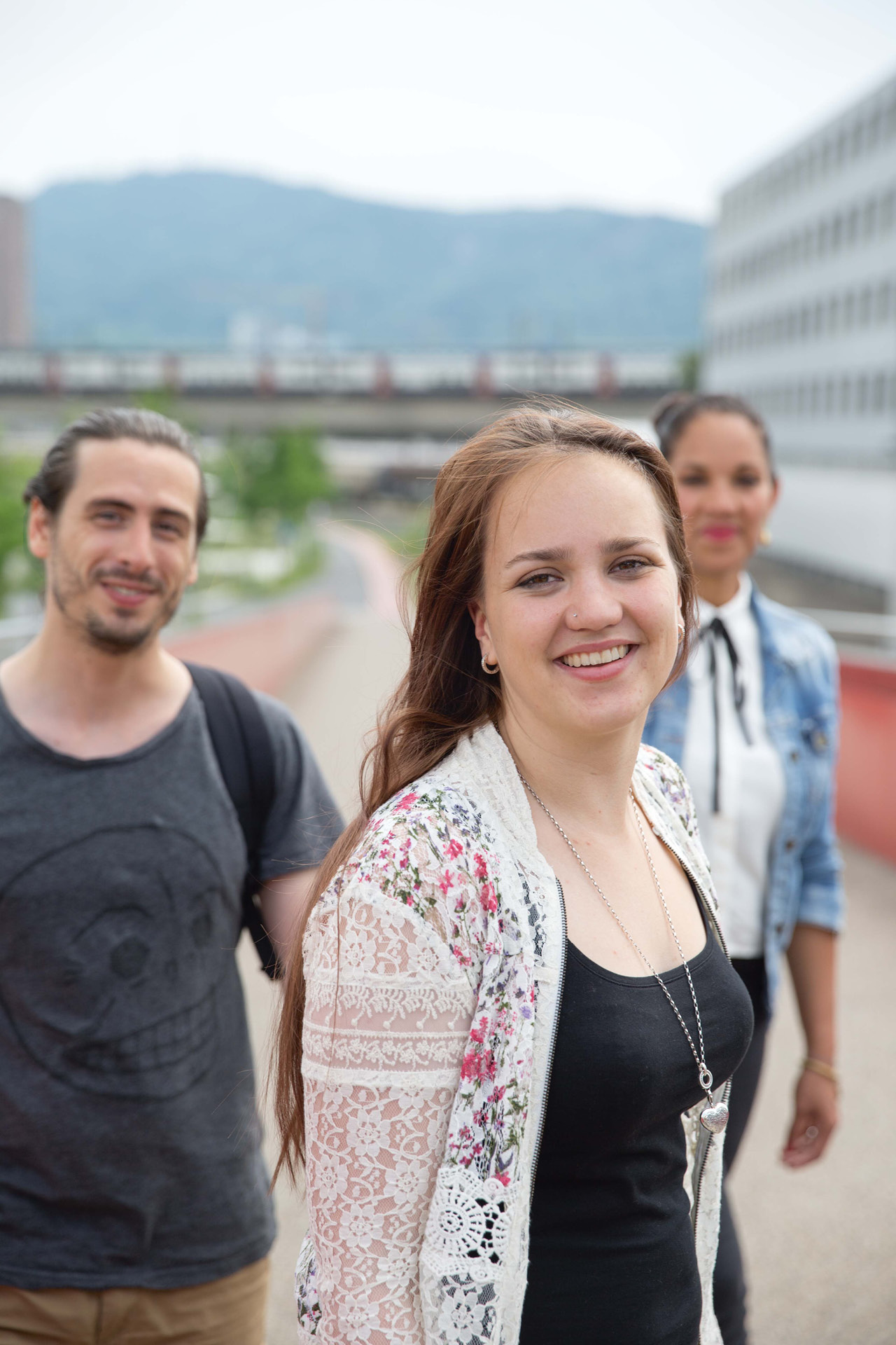 Drei fröhliche junge Personen laufen über eine Brücke in der Stadt.