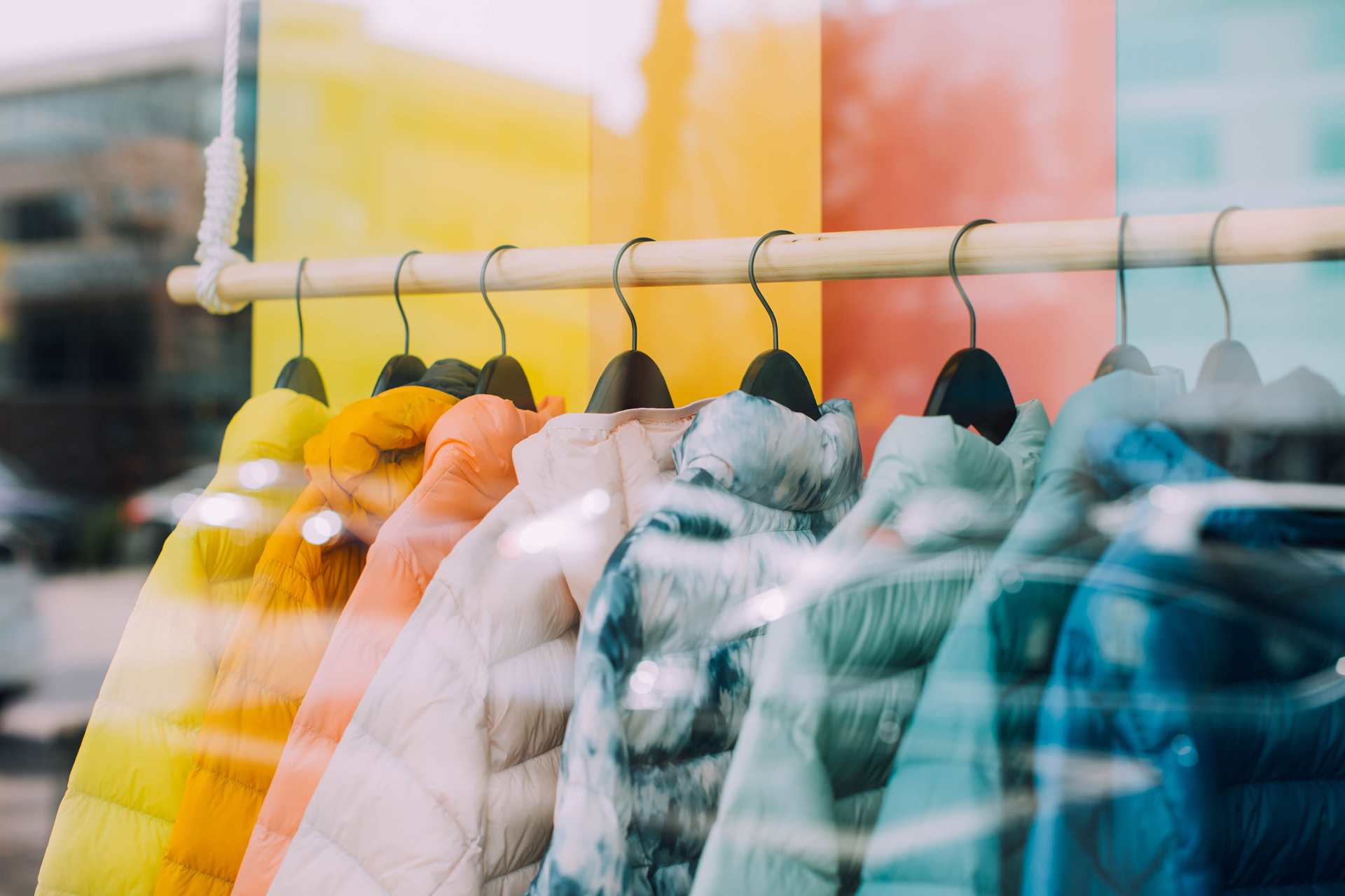 Im Schaufenster eines Modegeschäfts hängen Daunenjacken an Kleiderbügeln in allen Farben.