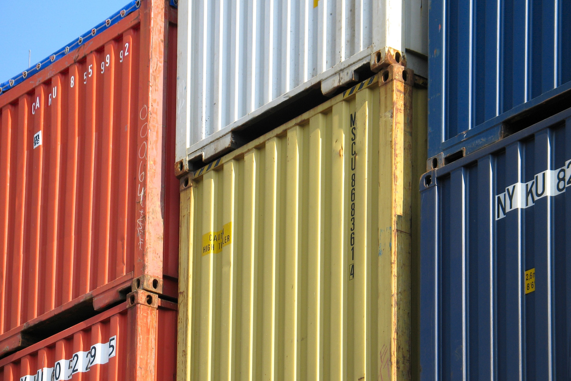 Farbige Schiffscontainer sind nebeneinander aufgestapelt.